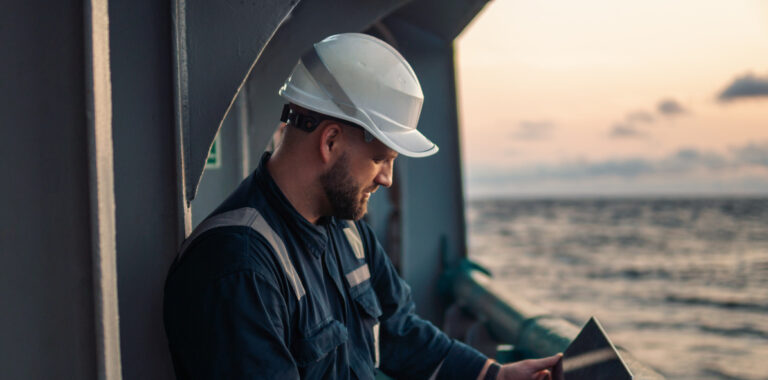 Marine chief officer or captain on deck of vessel or ship watching laptop